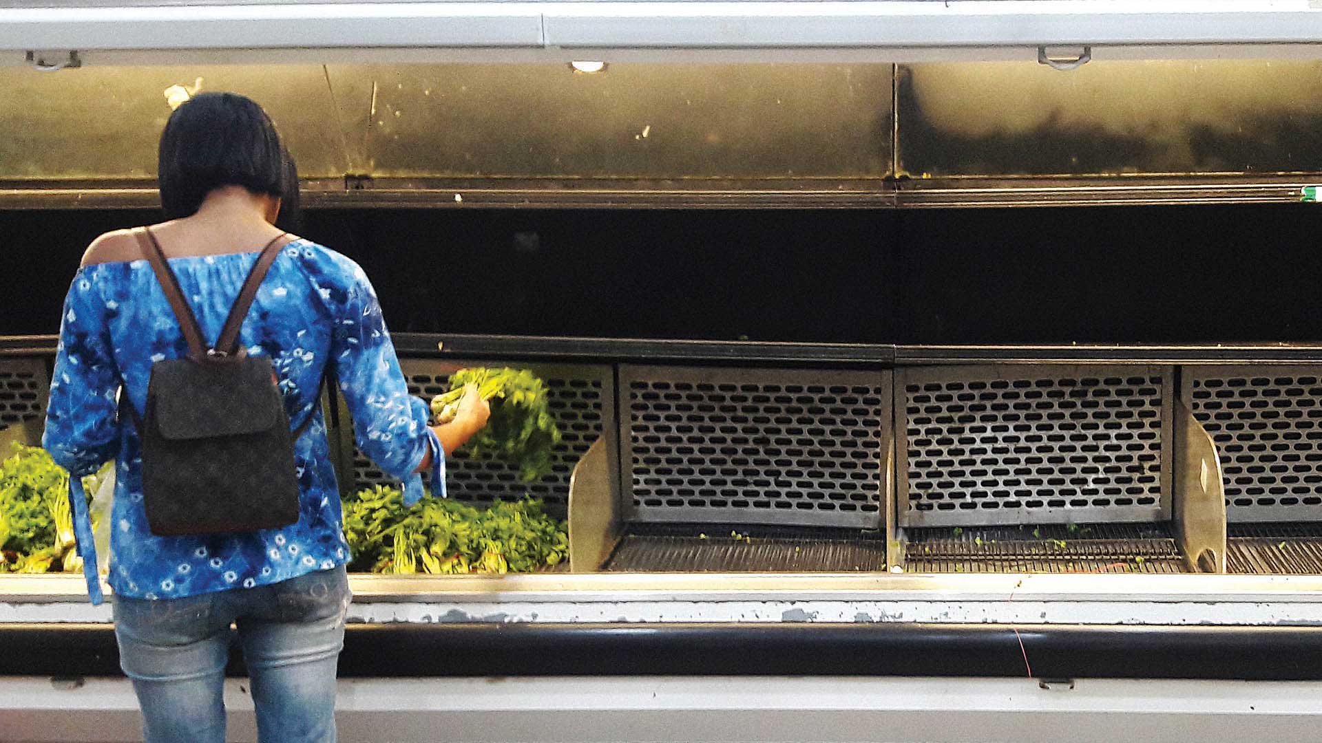Una mujer intenta hacer las compras en un supermercado en Caracas, entre góndolas y heladeras vacías. Foto: AFP.