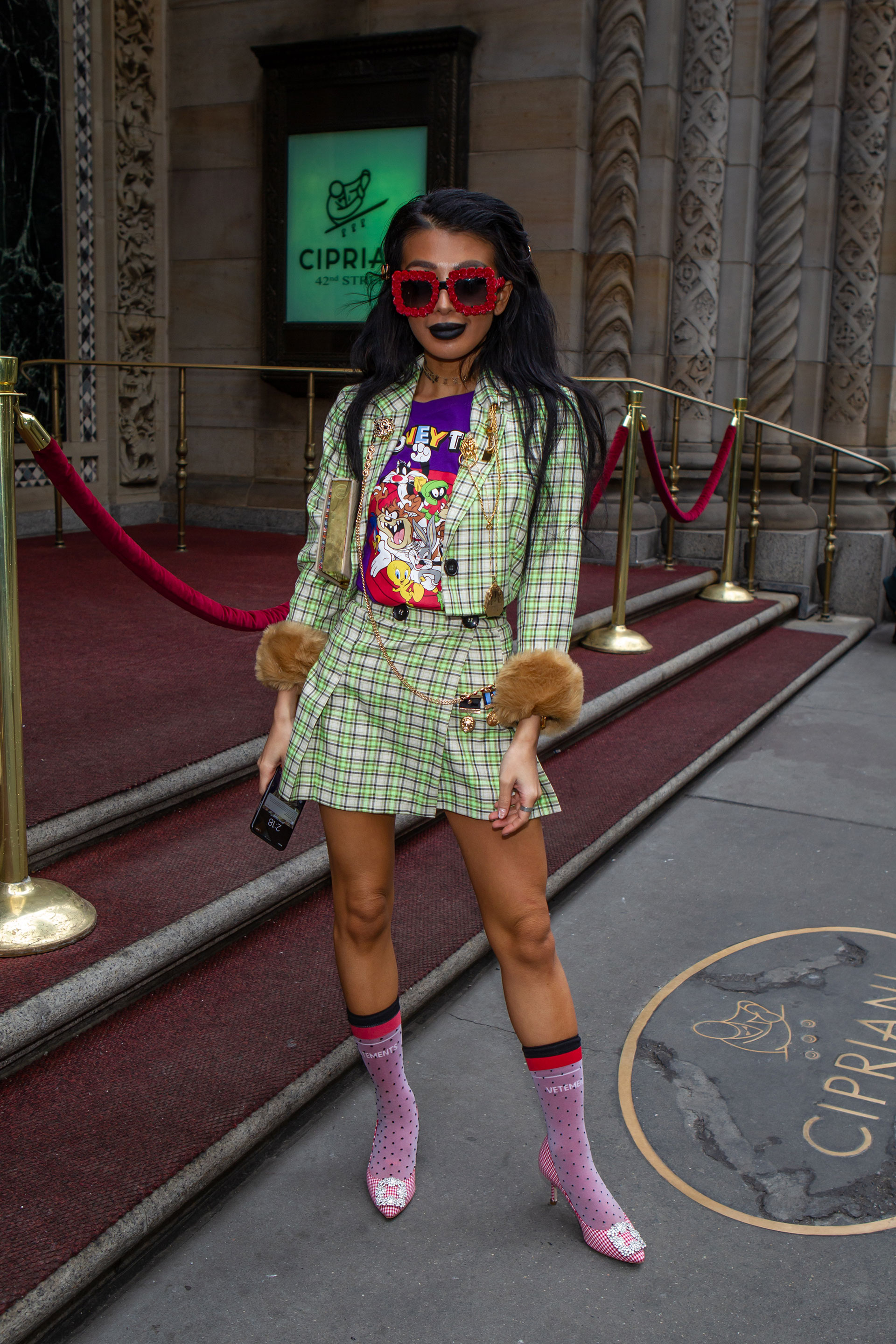 La combinación del tartán en flúor verde y blanco de falda y chaqueta con puños de piel marrón con remera estampada de los famosos dibujos de los Looney Toons. Como complemento de su look fashionista, unos anteojos XL y los clásicos Manolo Blahnik en rosa con medias 3/4 a lunares