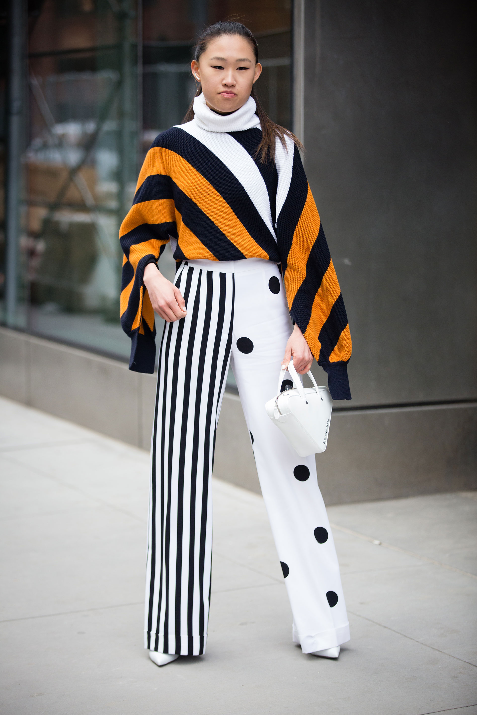 Dos tendencias, una prenda. La fashionista eligió las tendencias del rayado y los polka dots (lunares) en blanco y negro en un pantalón semi oxford tiro alto para combinarlo con un maxi sweater de punto rayado tricolor en naranja, negro y blanco, con cuello polera. Lo completó con la mini bag triangular de Balenciaga y stilettos en punta