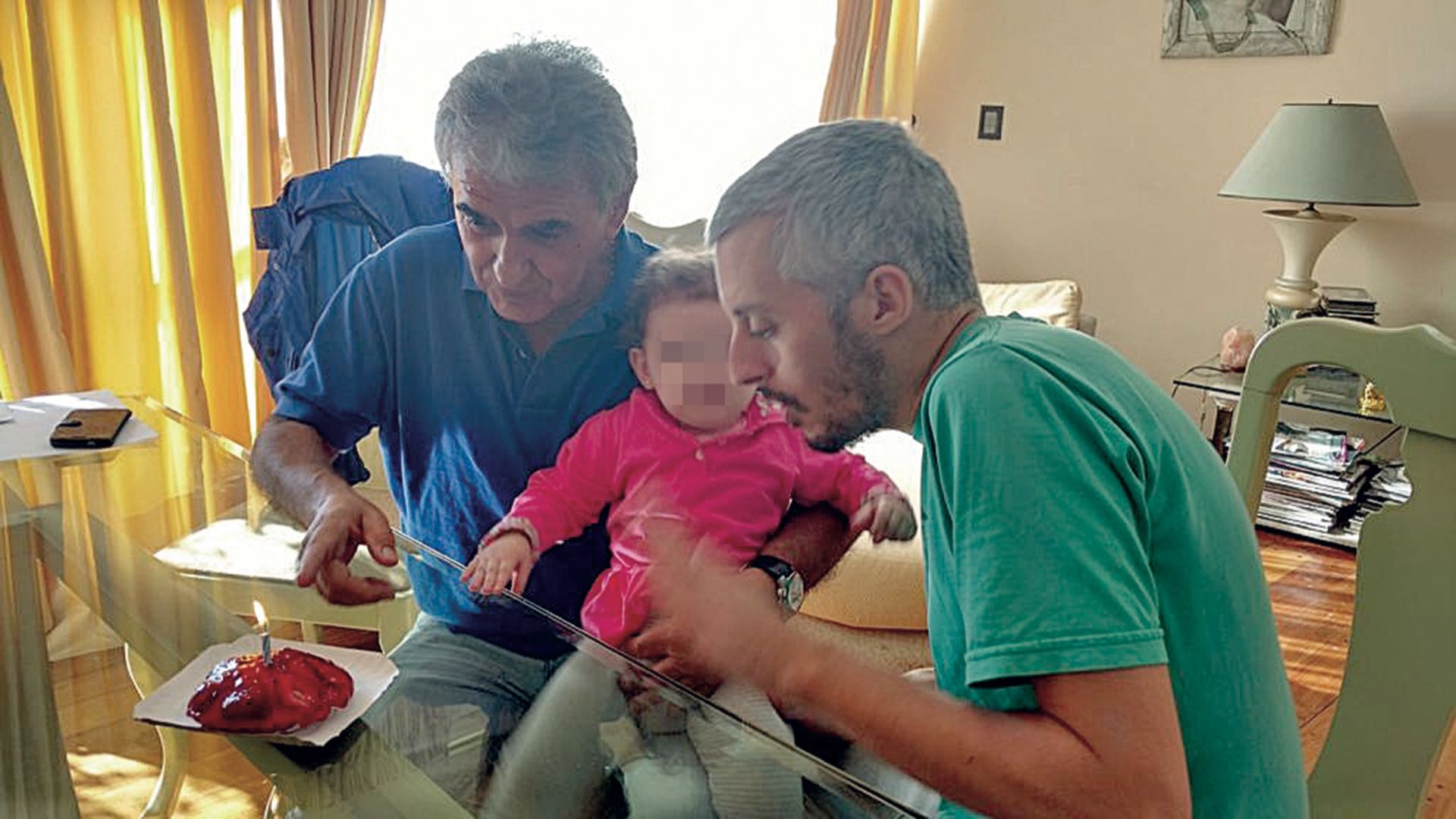 Víctima y victimario: El empresario Roberto Fernández en su último cumpleaños a punto de soplar las velitas, con su nieta a upa, y su homicida, su propio yerno, Santiago Corona, padre de la criatura, a su lado.