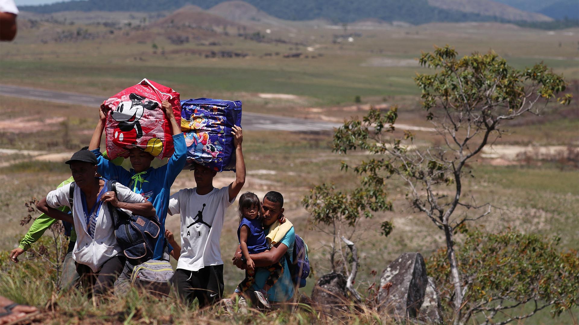 La gente camina con sus pertenencias a través de un campo, mientras intenta cruzar la frontera entre Venezuela y Brasil en Pacaraima, estado de Roraima (Reuters)