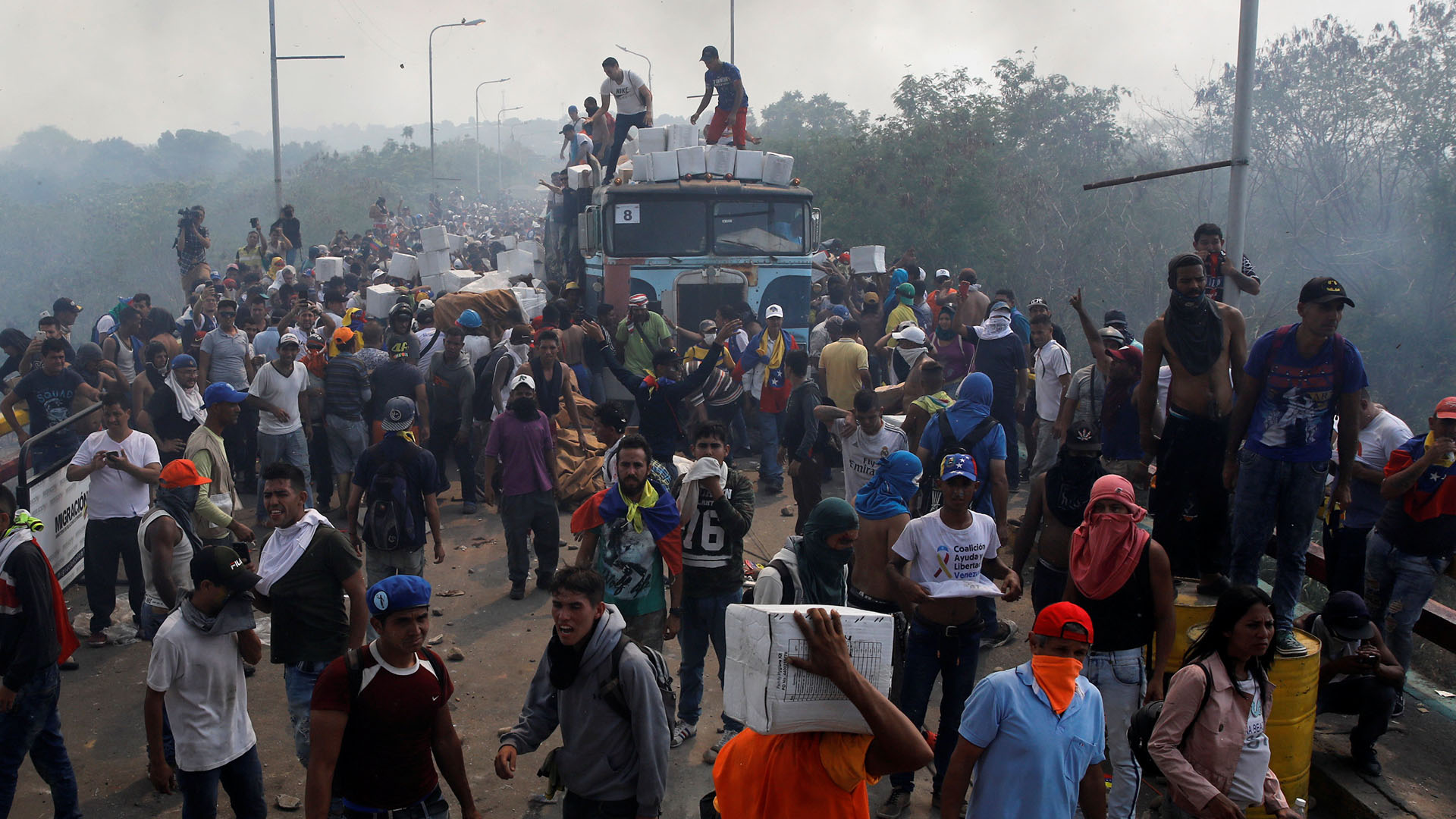 Opositores descargan alimentos de los camiones tras ser atacados por orden de Nicolás Maduro en uno de los pasos fronterizos (Reuters)