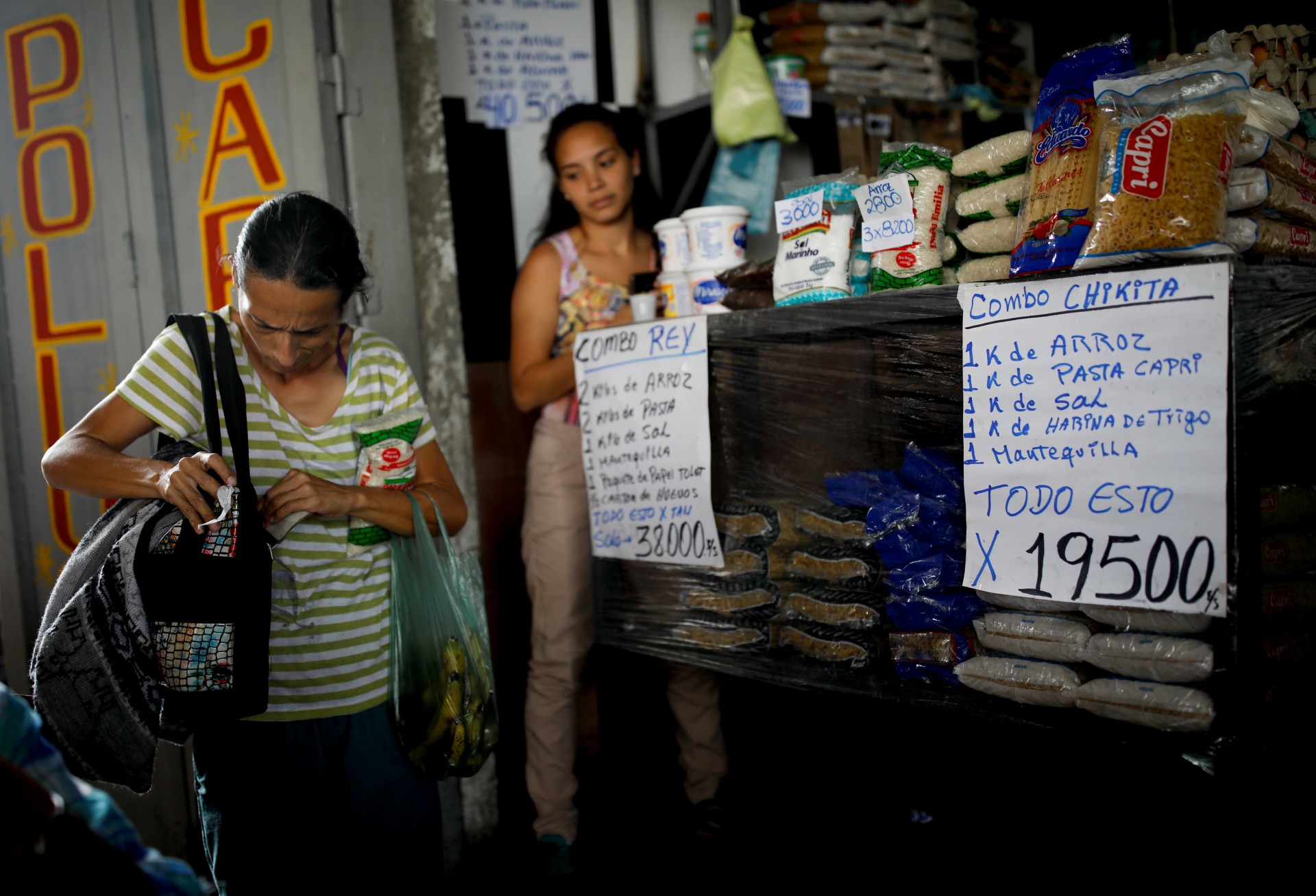 Yaneidi Guzmán, de 38 años, va a comprar comestibles en Caracas, Venezuela, 19 de febrero de 2019. Un letrero (derecha) anuncia una pequeña oferta combinada de un kilo de arroz, un kilo de pasta, un kilo de sal, un kilo de harina y Medio kilo de mantequilla por 19500 bolívares. El salario mínimo mensual en Venezuela es de 18000 bolívares.