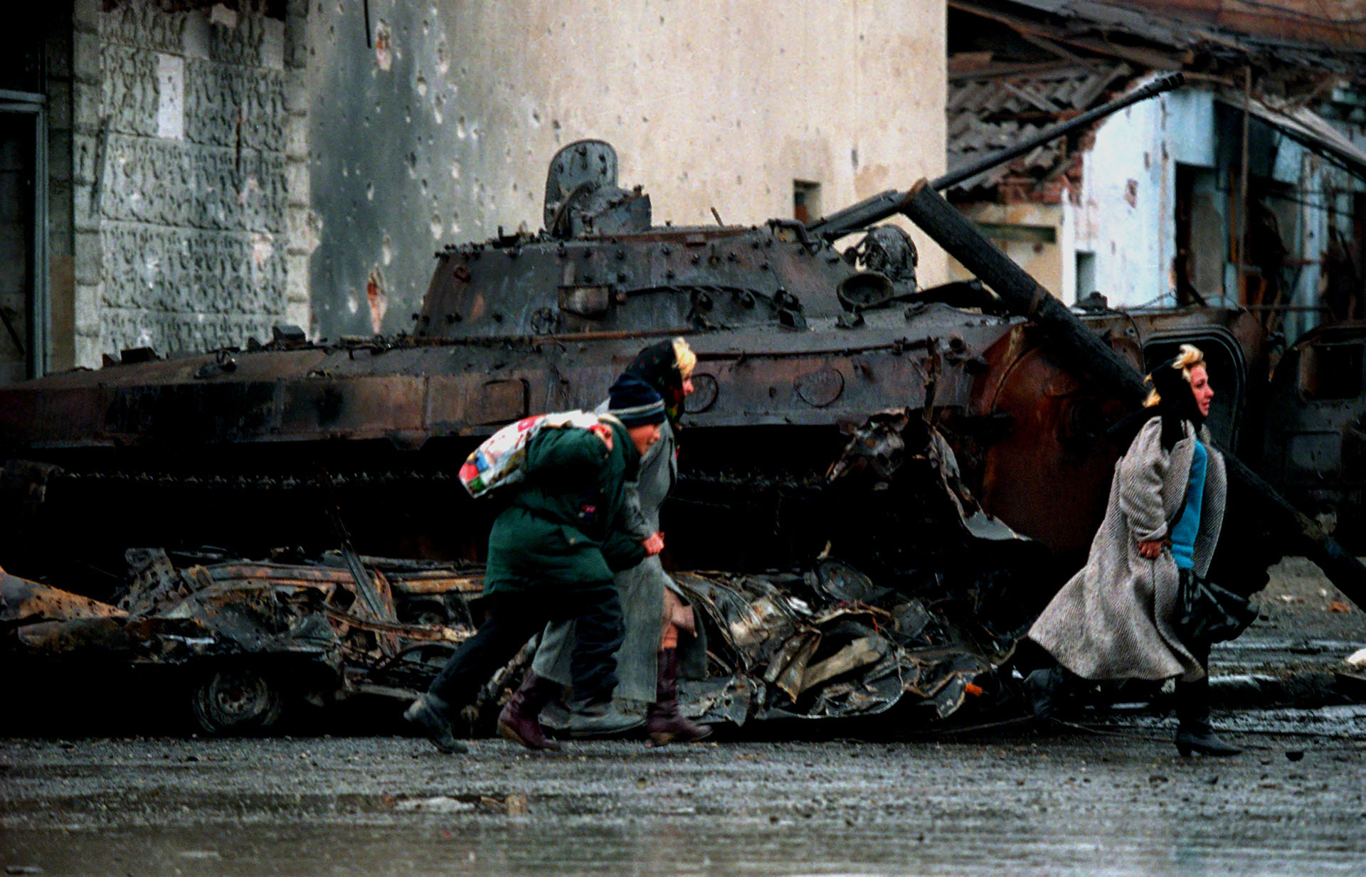 Civiles chechenos corren frente a un tanque ruso destruido en Grozny, durante un enfrentamiento en enero de 1995