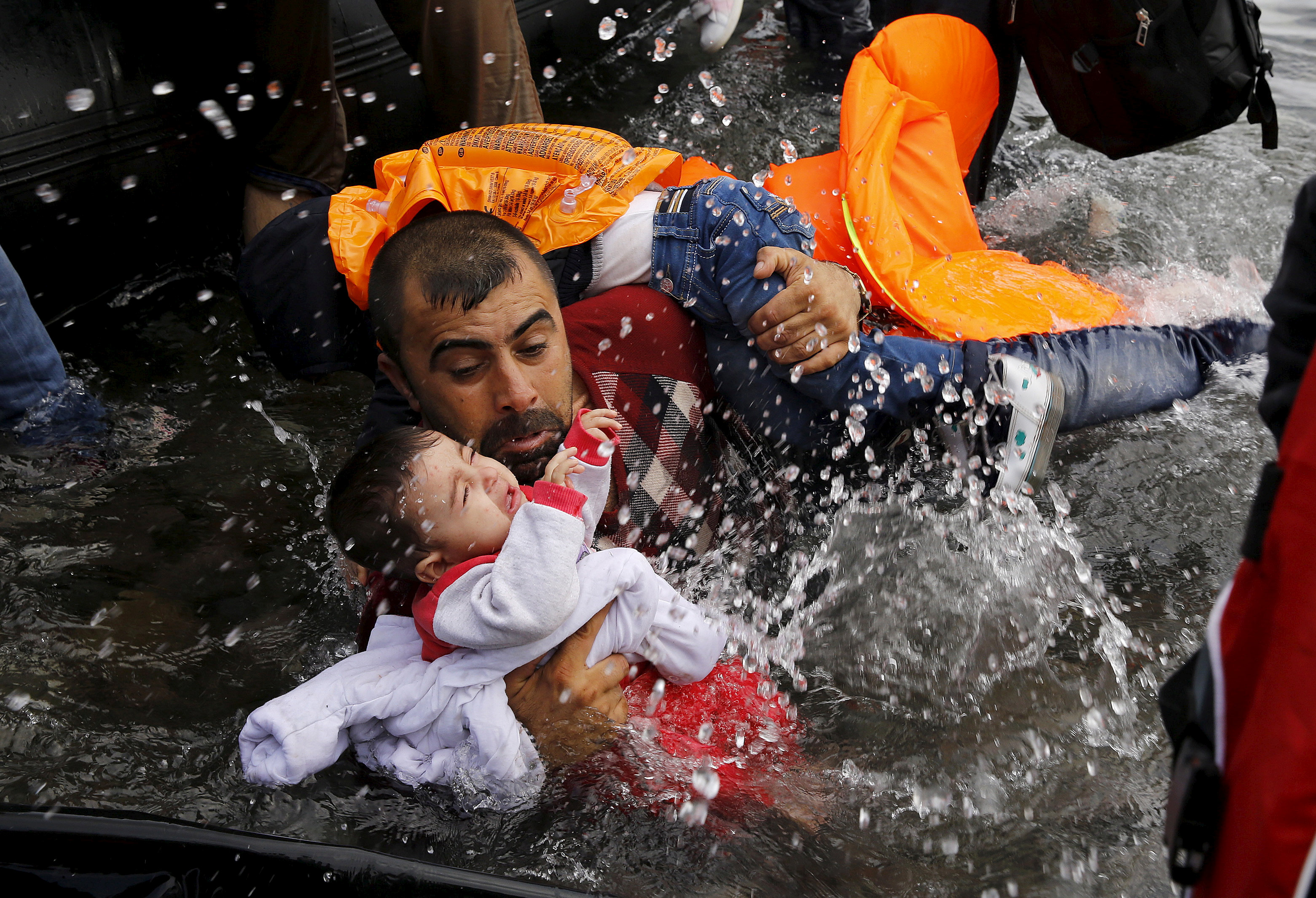 Un refugiado sirio lucha por mantener a flote a sus hijos al bajar de una embarcación en la isla griega de Lesbos