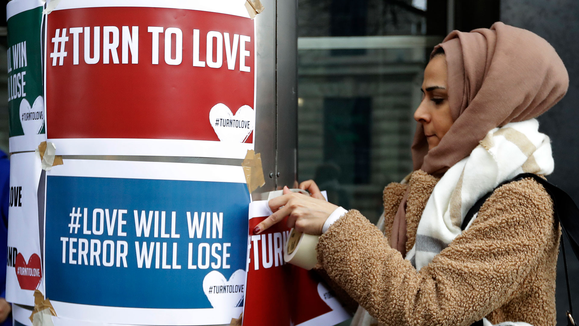Un manifestante cuelga pancartas del grupo ecuménico ‘Turn to Love’ (Volver al amor) en una vigilia en la Casa de Nueva Zelanda en Londres (Foto: AP)