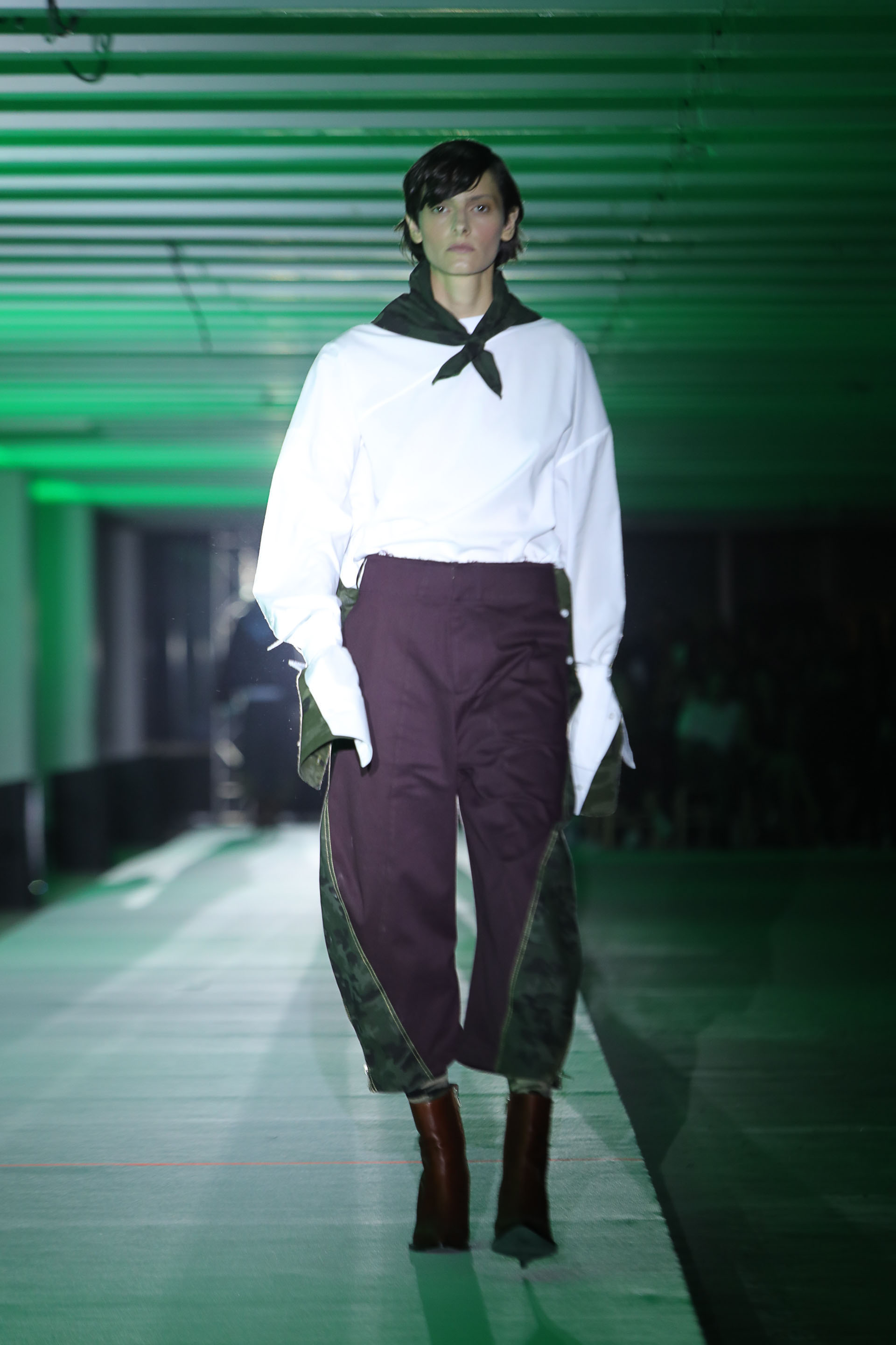 Un tradicional buzo de JT blanco con mangas XL combinado con tela impermeable verde. Para completar el look, pantacourt bicolor violeta y verde impermeable. Como accesorio, un pañuelo en su cuello