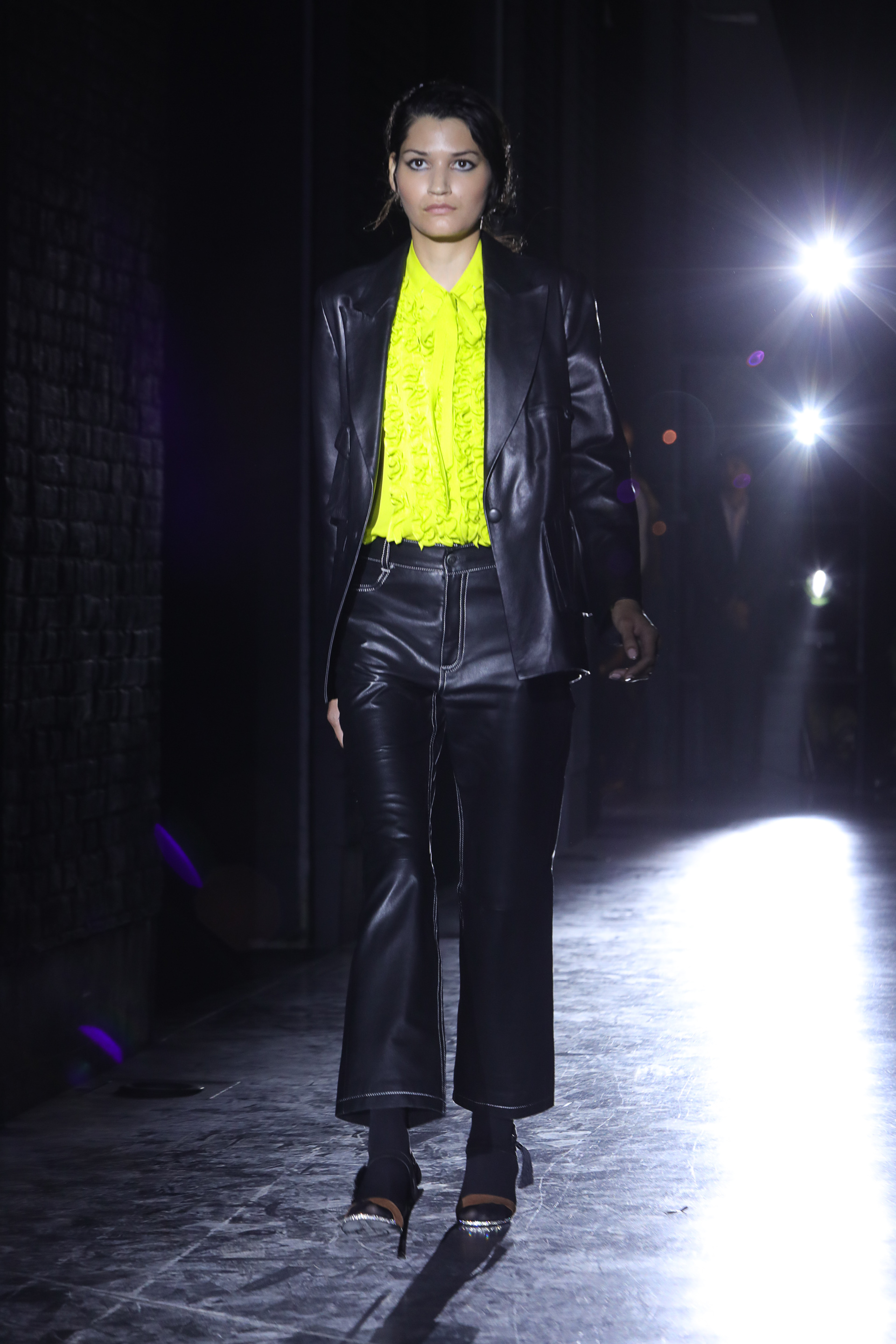 Los conjuntos de pantalón y saco de la nueva colección son de cuero de oveja elastizado. En pasarela, el look combinado es en color negro con detalles de hilo blanco. La blusa con jabot en verde lima.