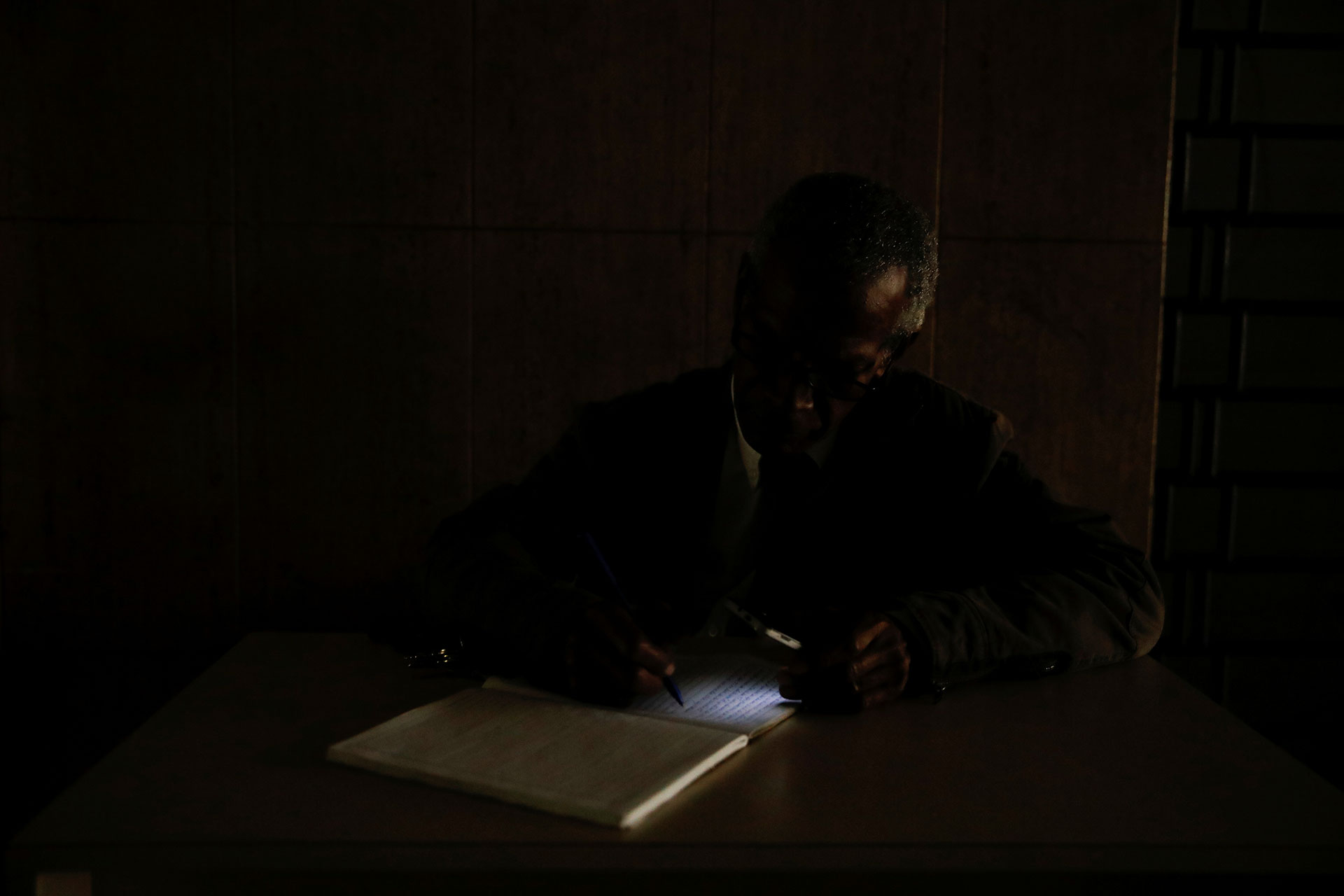 Un guardia de seguridad usa la linterna de su celular para iluminar un libro durante el apagón masivo en Venezuela (Reuters)