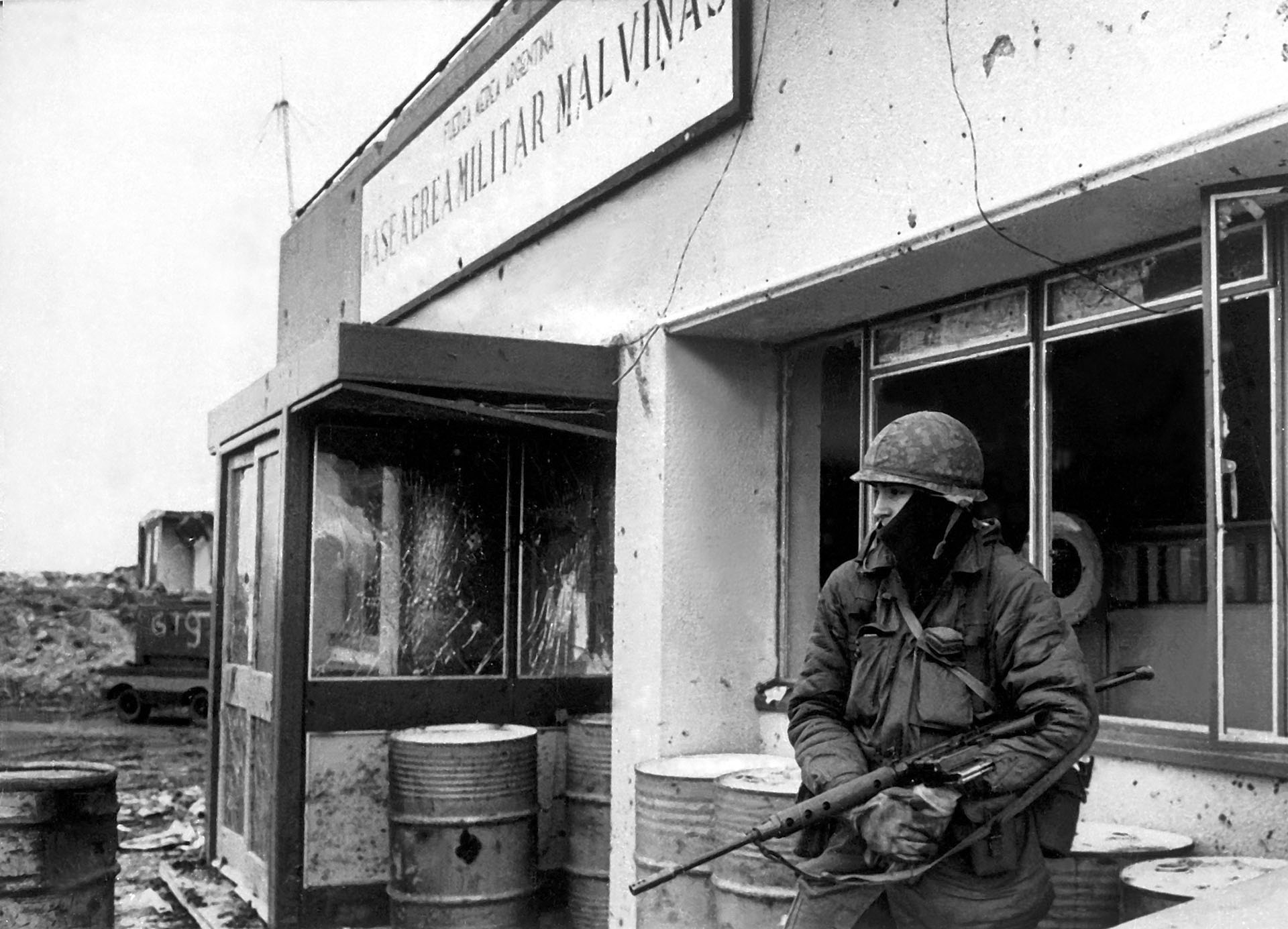 Estoico, en soledad, el soldado custodia la entrada de la Base Militar Malvinas. Los vidrios de las ventanas están hechos añicos o han desaparecido por los efectos de las bombas. Los tambores de gasolina le sirven como apoyo (Foto: Eduardo Farré).