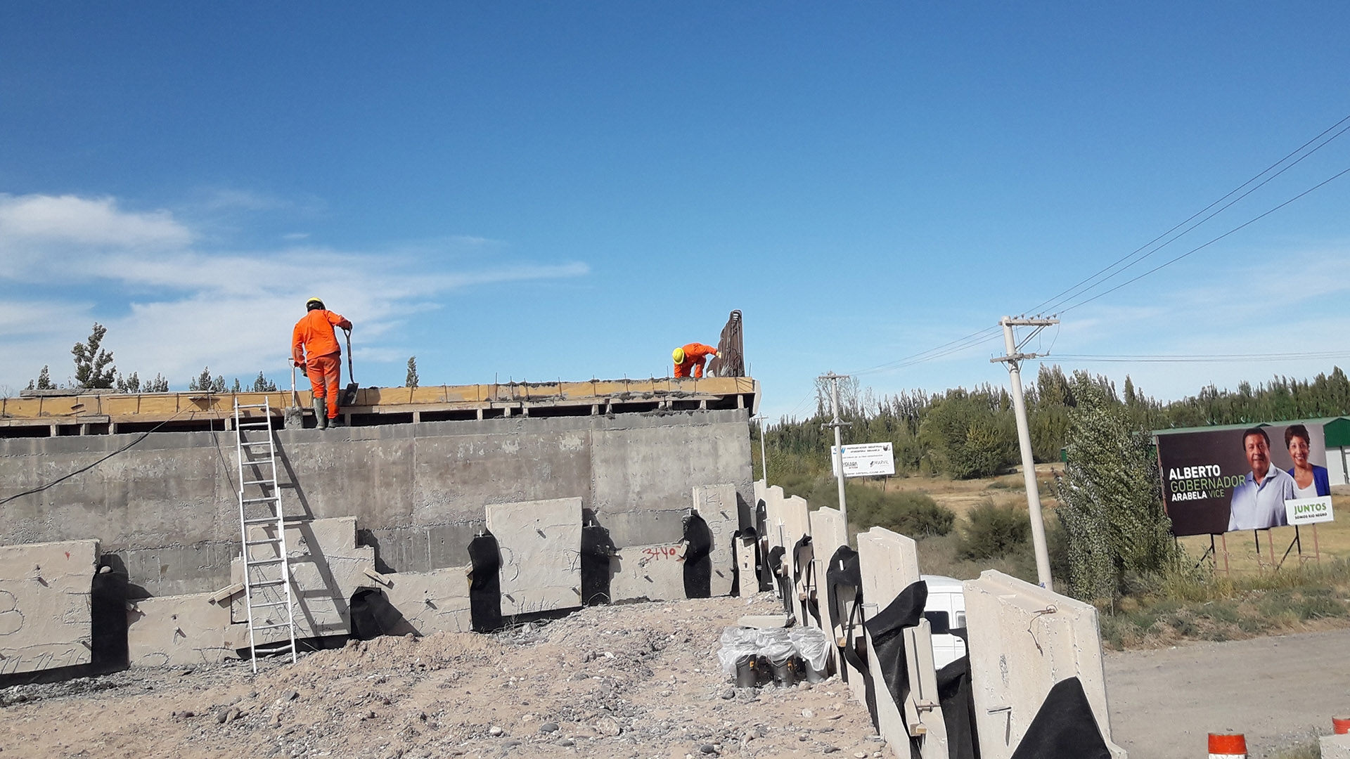 Los afiches de Weretilneck y Carrera este sábado al lado del puente en construcción que se reactivó