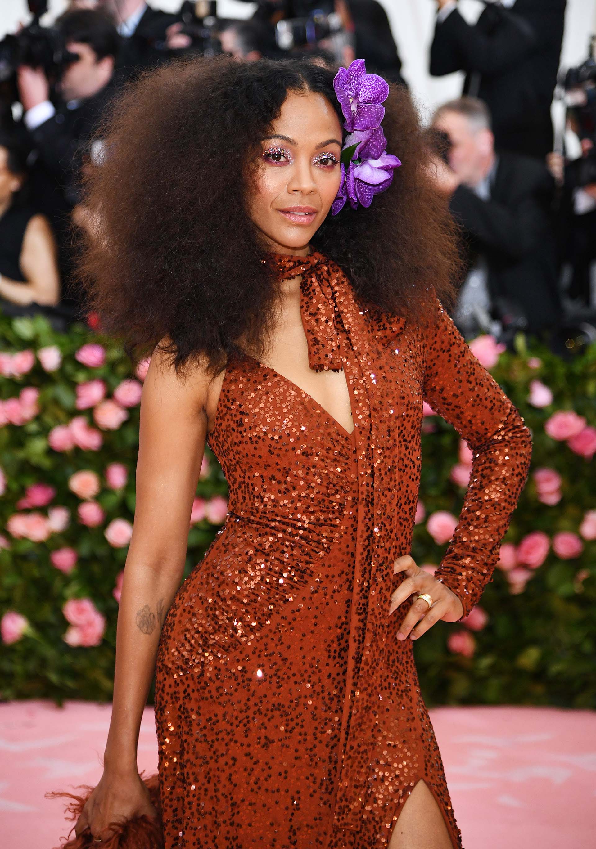 La actriz Zoe Saldana vistió un traje de lentejuelas color ladrillo de una manga con un detalle de flores violetas hawaianas en el cabello