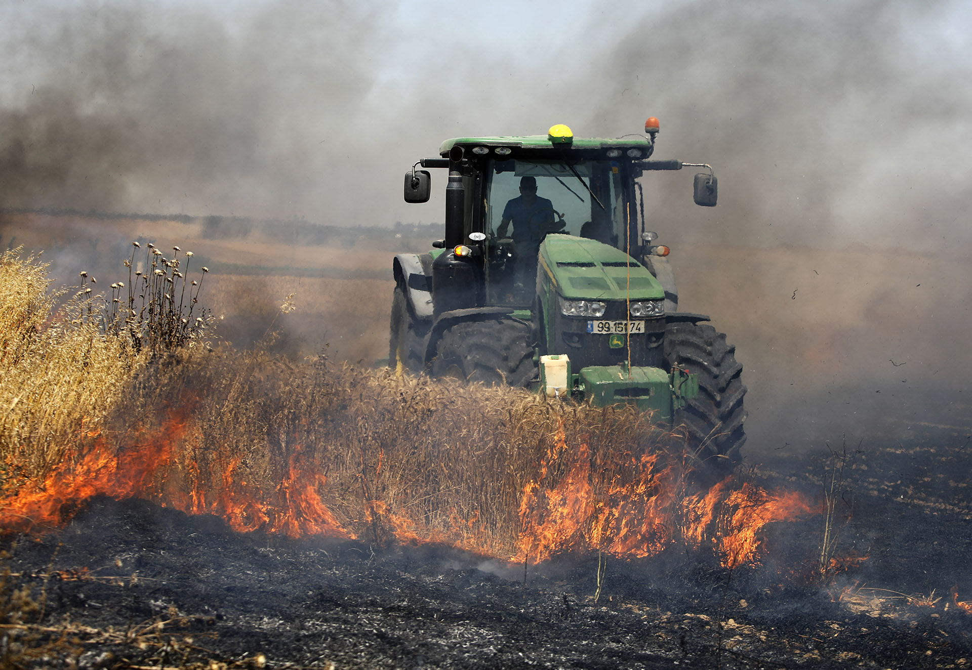 Un agricultor israelí maneja su tractor en medio de un incendio causado por protestantes palestinos. (Menahem KAHANA / AFP)