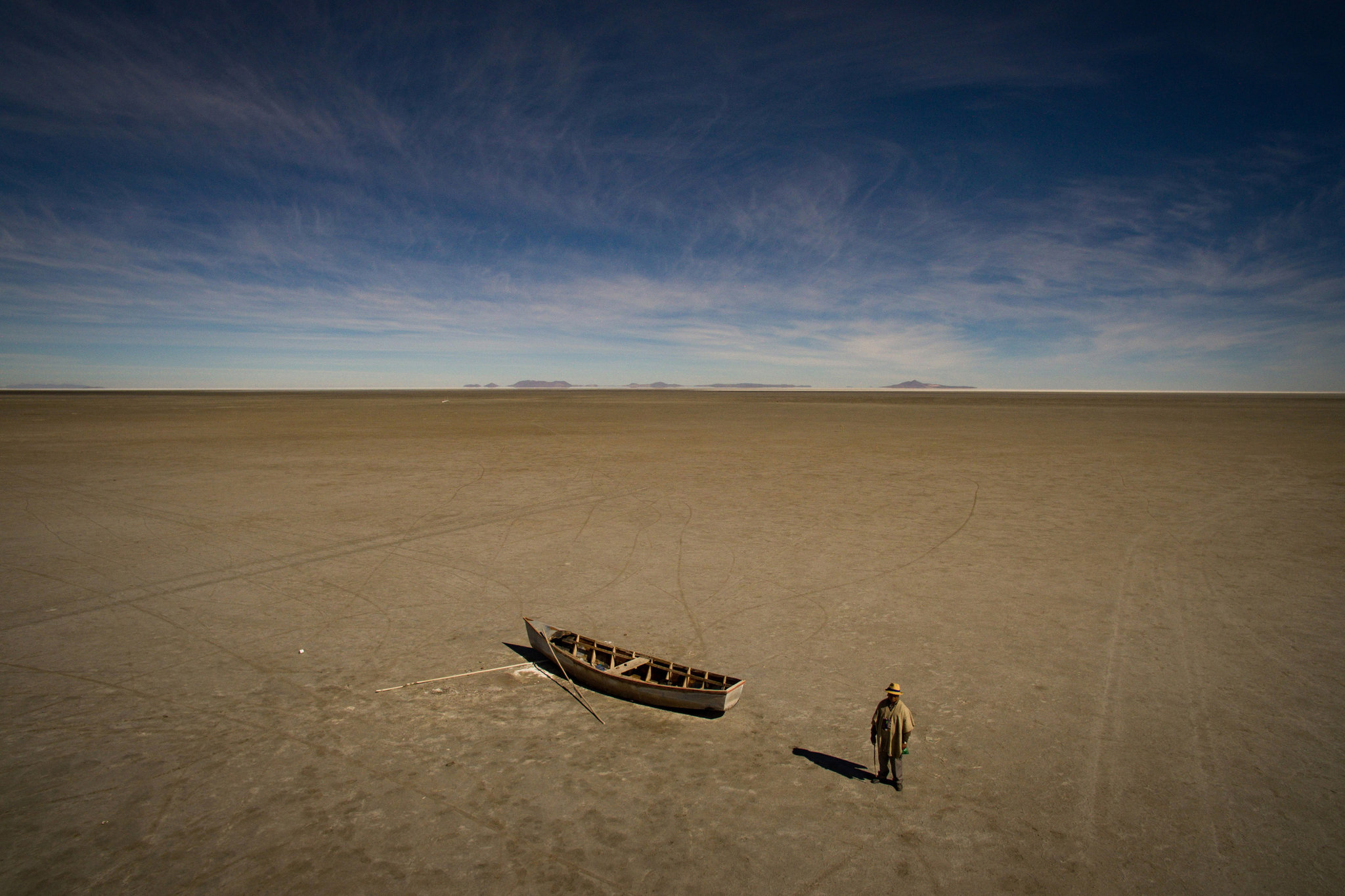 Félix Condori, de 31 años, alcalde de Llapallapani que antes trabajaba como pescador, junto a un bote en el lecho seco de lo que alguna vez fue el segundo lago más grande de Bolivia. Ahora debe viajar para encontrar trabajos de construcción como medio para ganar dinero puesto que el lago que definió su cultura y sustento ya desapareció. Mayo de 2016. (Josh Haner/The New York Times)
