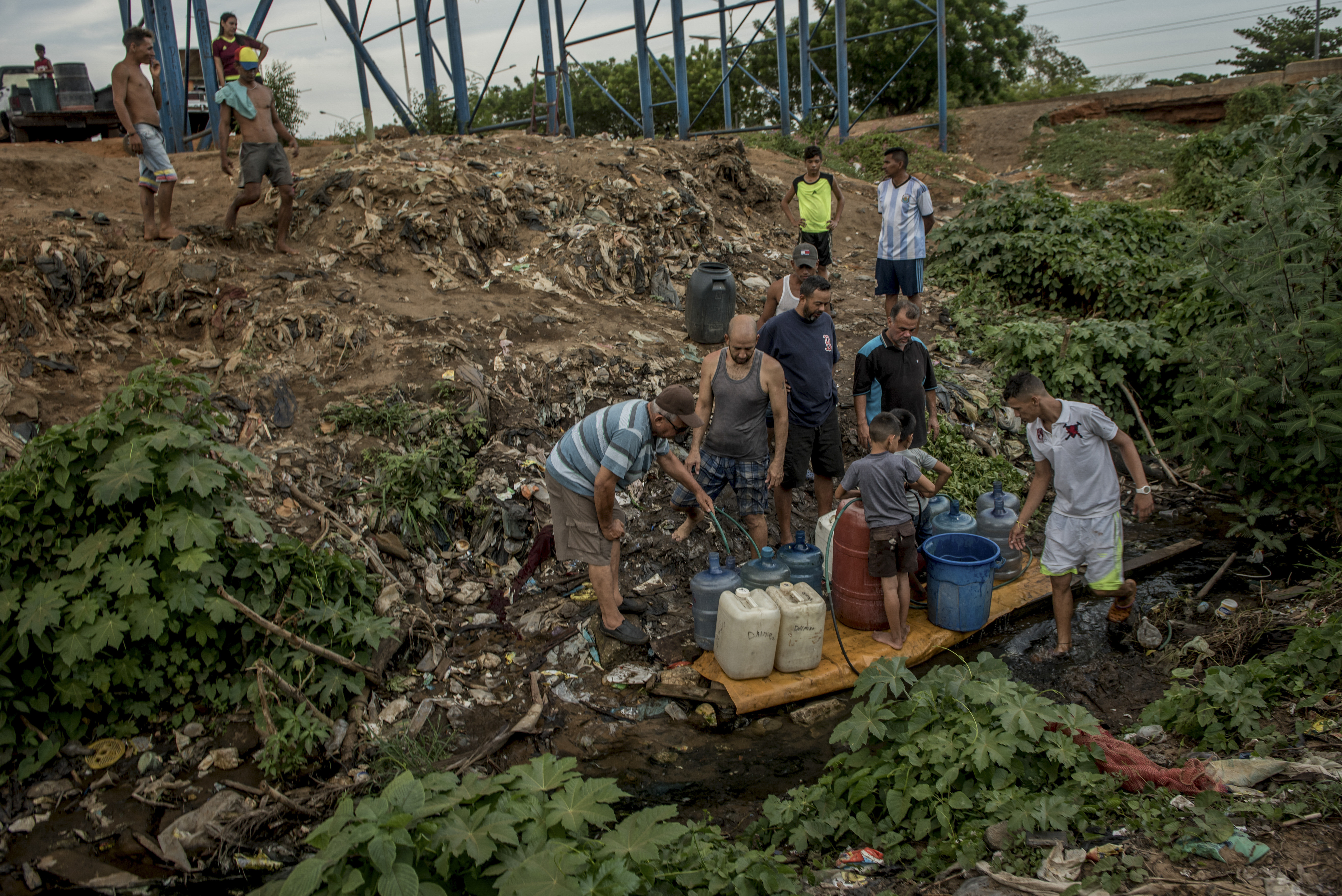 Un grupo de hombres llenaban envases de plástico con agua de un arroyo sucio, su única fuente de líquido durante los días en que no les llega el suministro. (Meridith Kohut/The New York Times)