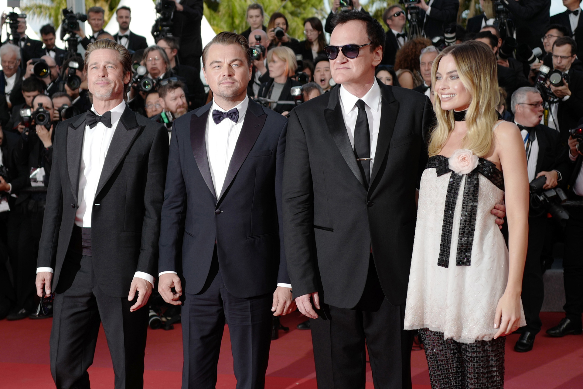 Brad Pitt, Leonardo DiCaprio con black tie de moño Quentin Tarantino y black tie de corbata y Margot Robbie con vestido corto y pantalón de lentejuelas con detalle de rosa rosada en el borde del vestido. Como accesorio, una gargantilla de chiffón