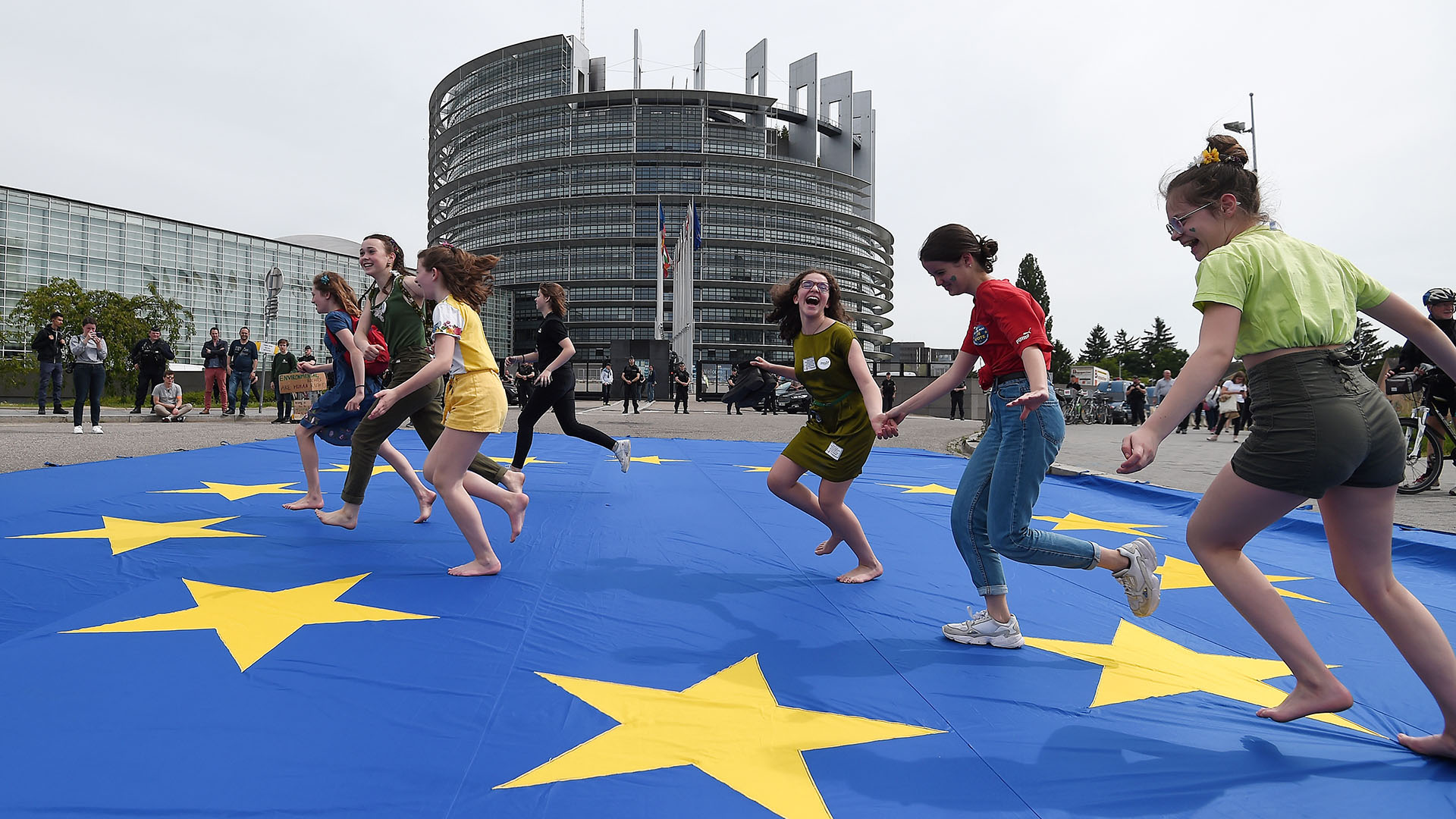 Jóvenes corren sobre una bandera europea gigante mientras participan en una protesta exigiendo acción urgente contra el calentamiento global, el 24 de mayo de 2019, ante el Parlamento Europeo en Estrasburgo, al este de Francia. (AFP)