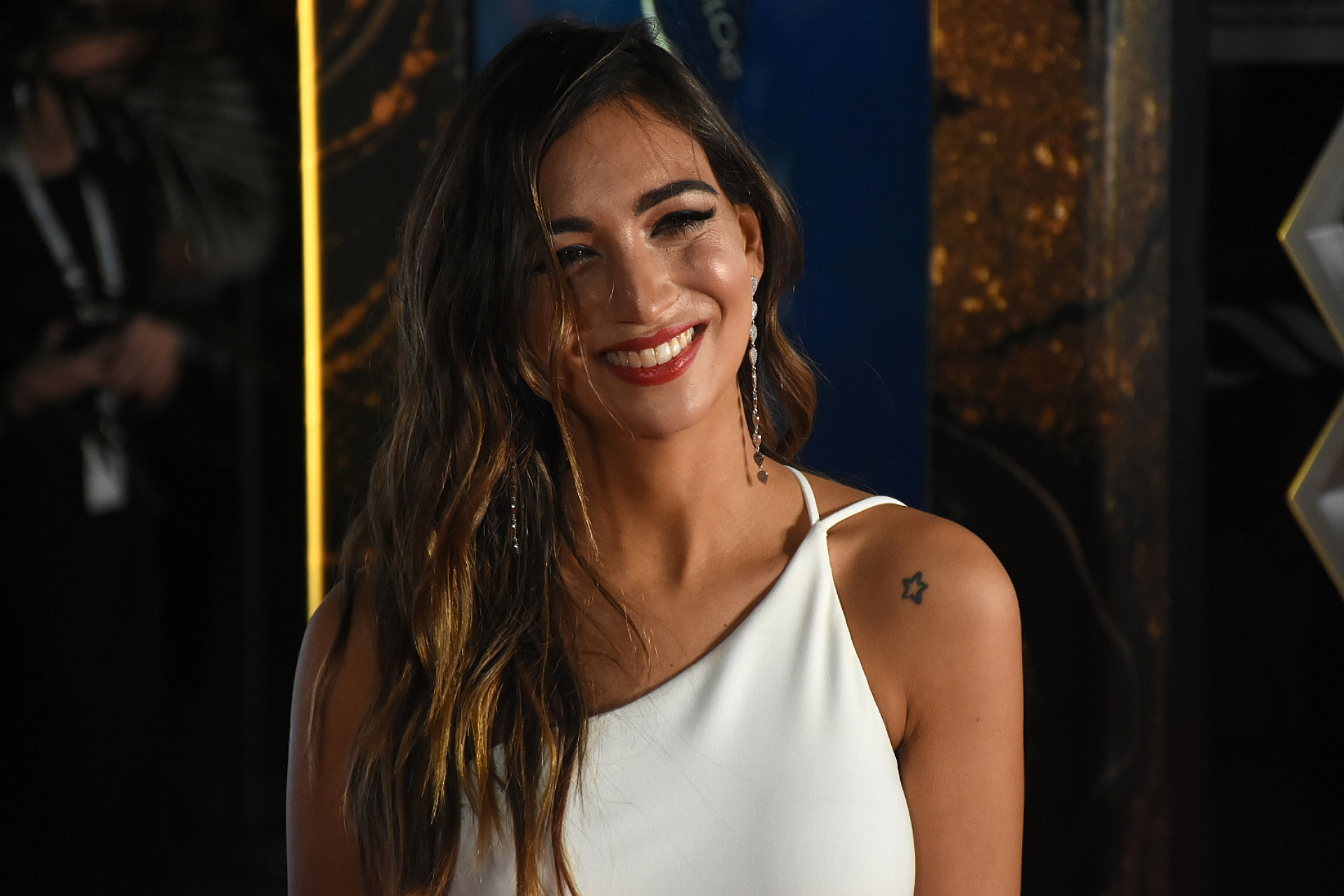 Camila Hadad con vestido de Nachi Gallo de crepe de seda natural en blanco de un solo hombro y un gran tajo. Completó su look con accesorios en plateado y maquillaje resaltando los labios en color rojo. Estilismo por Romina Giangreco
