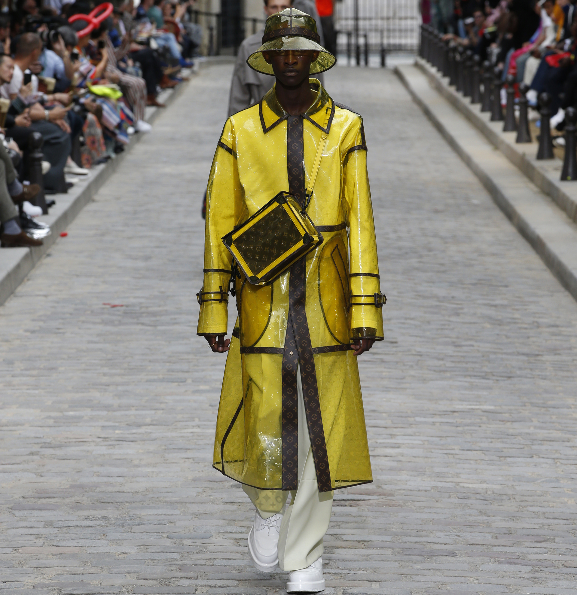 Uno de los protagonistas de la colección de Louis Vuitton fue el impermeable con el logotipo de la marca. De corte midi y con el sombrero haciendo juego, el look lo completó una crossbody en amarillo con el monogram en marrón