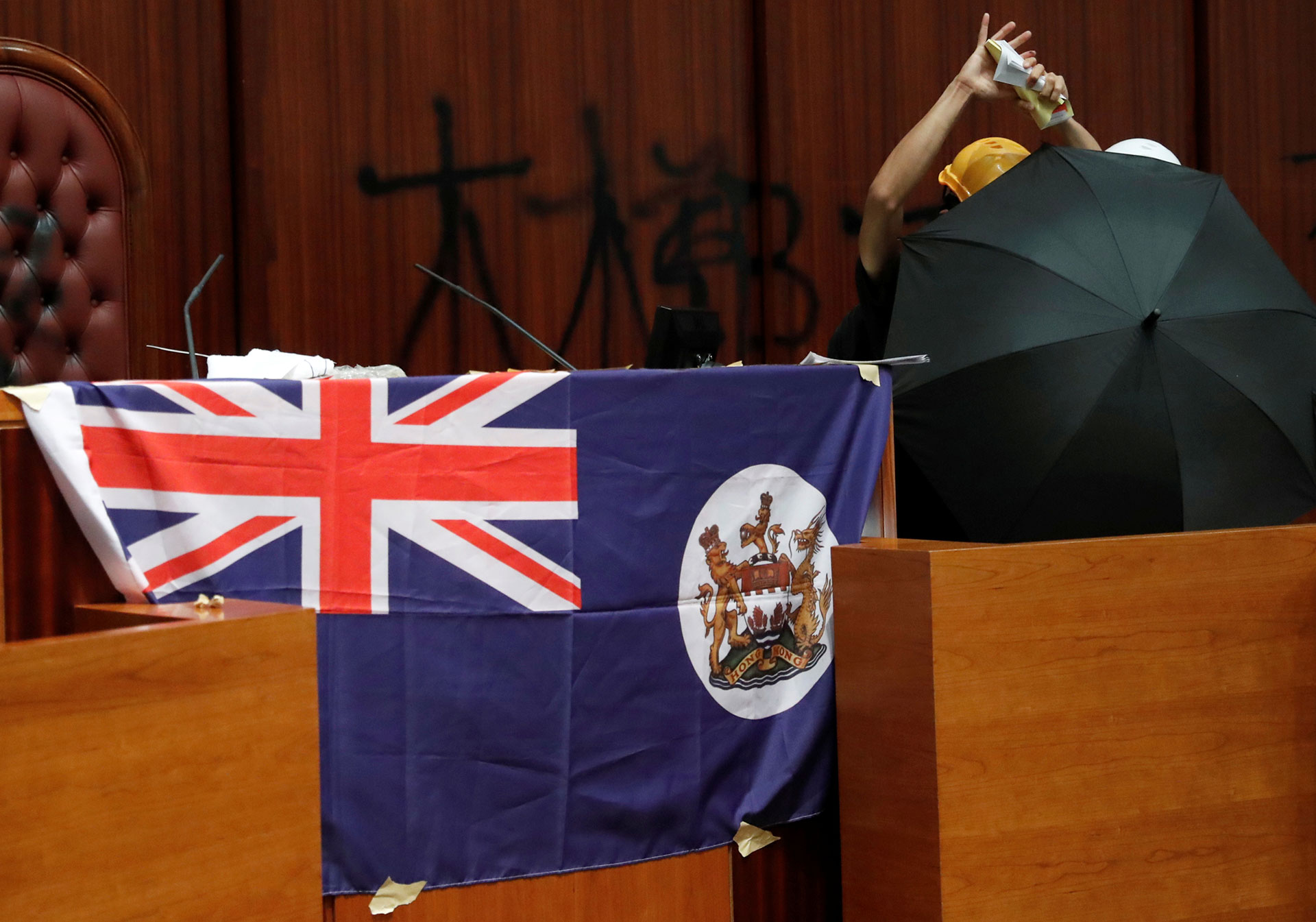 Una persona rasga un libro de la Ley Básica de Hong Kong mientras está al lado de una bandera colonial del país desplegada dentro de la cámara legislativa. (Reuters/ Tyrone Siu)