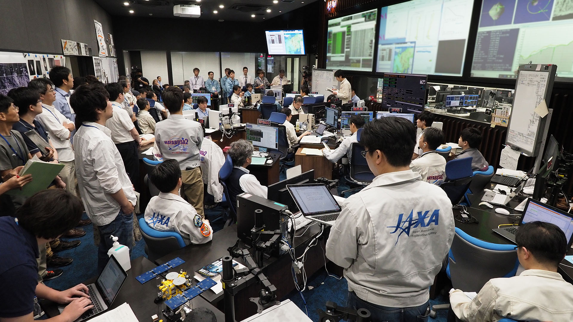 Investigadores y empleados, realizando una sesión informativa en la sala de control de la misión Hayabusa 2 en la ciudad de Sagamihara (Foto de Yutaka IIJIMA / ISAS-JAXA / AFP)