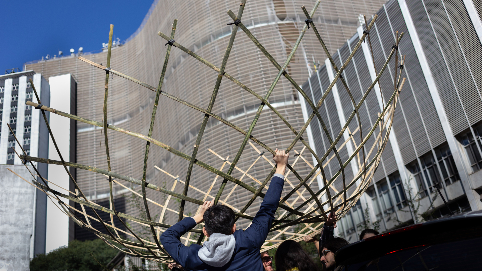 Los estudiantes del taller High Line Paulista cargan un domo de bambú frente al edificio Copan de Oscar Niemeyer en el centro de São Paulo. (Gabriela Portilho para The New York Times)
