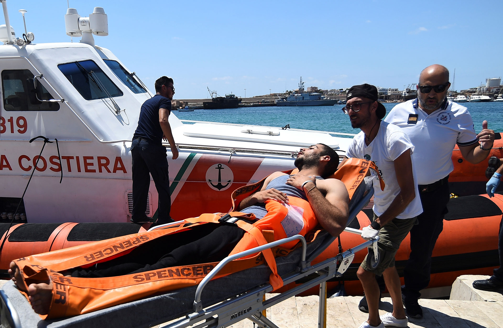 Un migrante que saltó del barco de rescate español es llevado en una camilla, en Lampedusa, Italia (REUTERS/Guglielmo Mangiapane).
