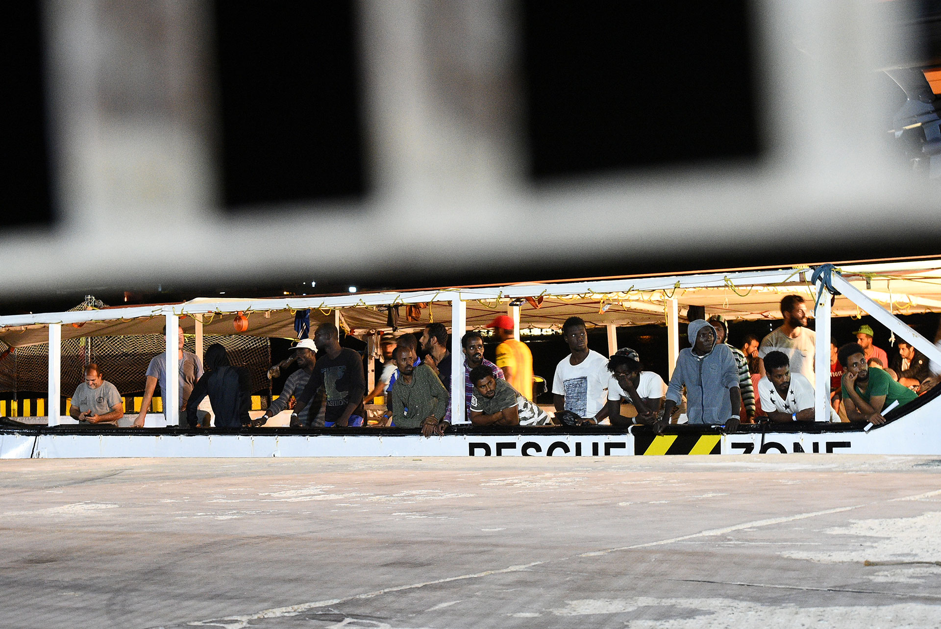 Migrantes miran desde el barco de rescate español al arribar a la isla italiana (REUTERS/Guglielmo Mangiapane)