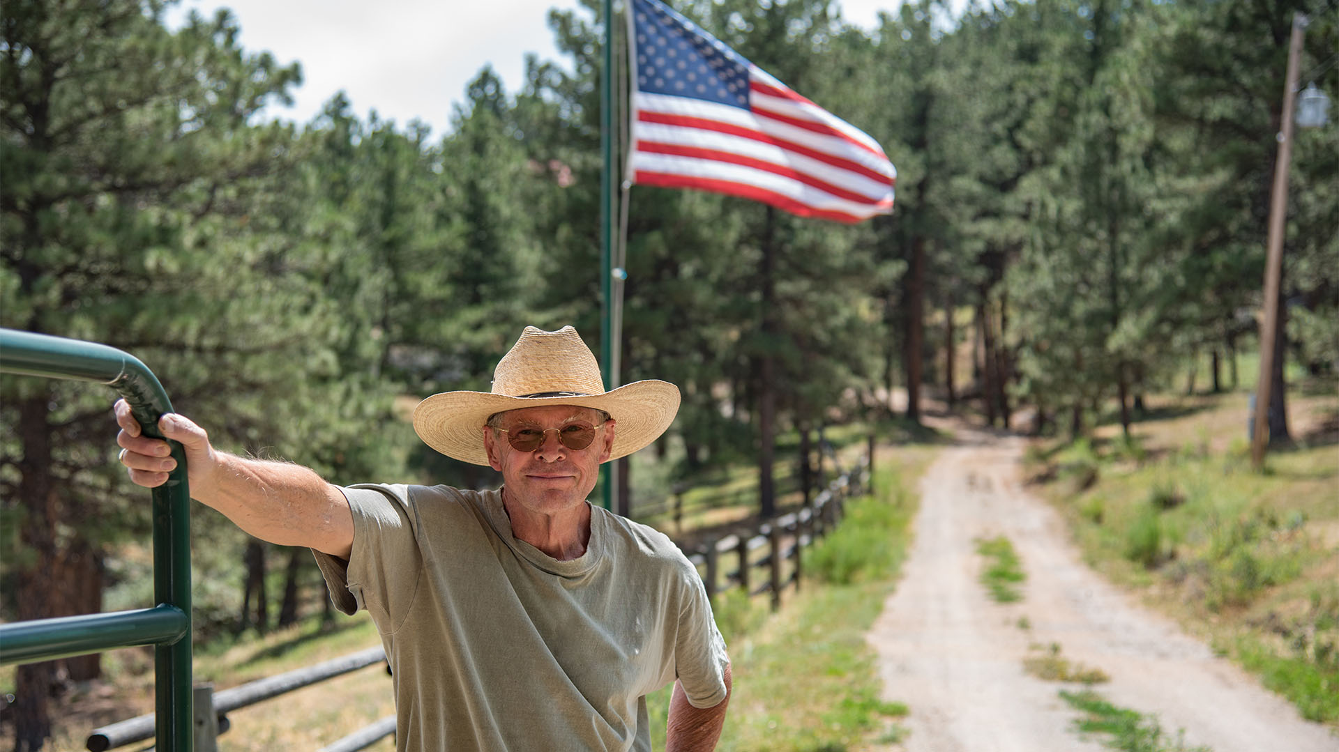 Un vaquero de Colorado con la mano en una puerta de metal verde con la bandera de Estados Unidos al fondo (Shutterstock)