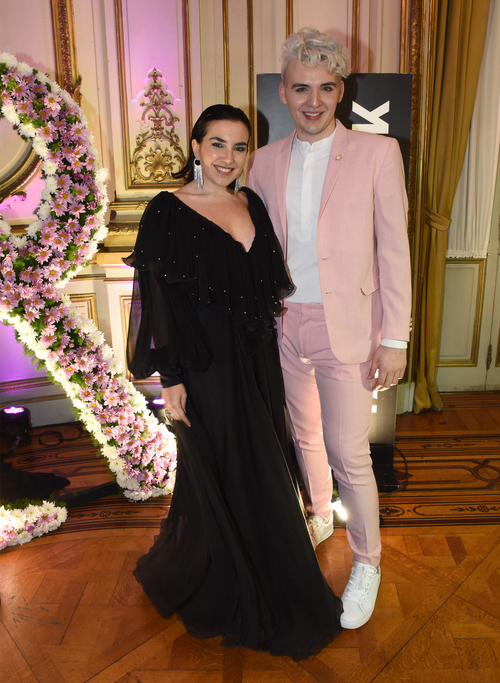 El diseñador Jorge Rey con su esmoquin rosa y zapatillas blancas y Lucía Ugarte, influencer de moda con un vestido de gasa negro y mangas abullonadas