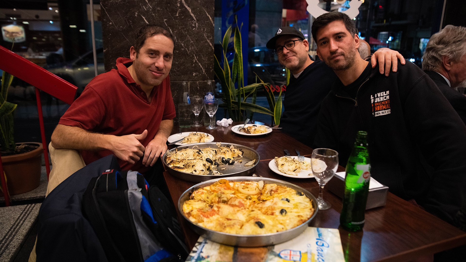 Amigos en Banchero disfrutando una fugazzetta y otra napolitana, dos clásicas de la tradicional pizzería de la Avenida Corrientes