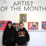Two Women standing in front of a wall with four drawings