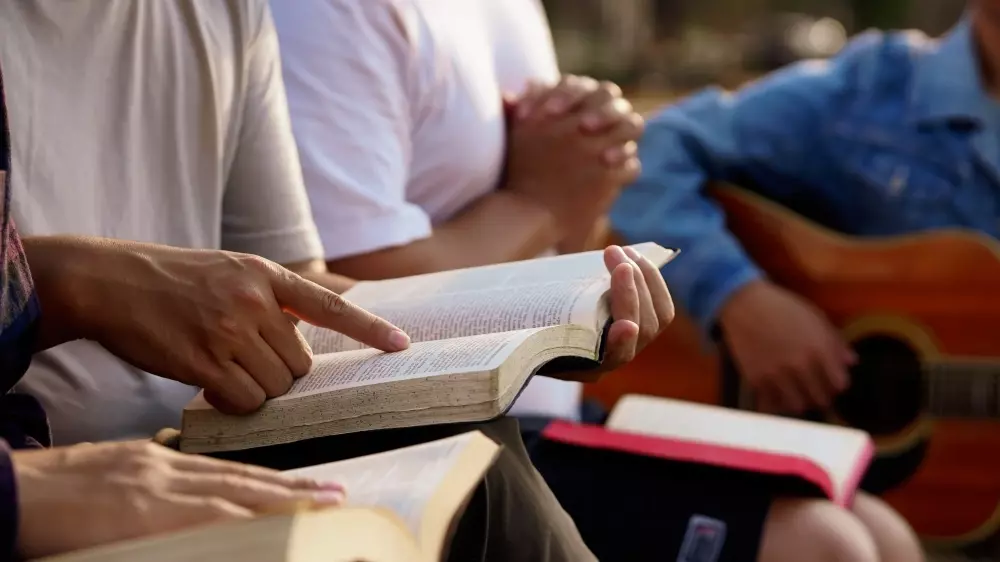 Hands holding the Bible and other in a prayer gesture