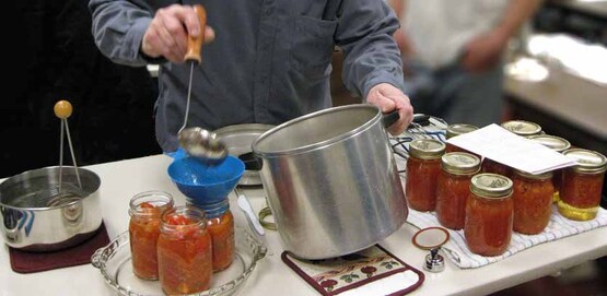 Putting hot tomatoes into a sterilized canning jar for hot water bath processing.