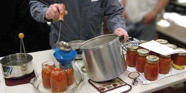 Putting hot tomatoes into a sterilized canning jar for hot water bath processing.