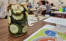 A picture of a class with a jar of pickles on the table.