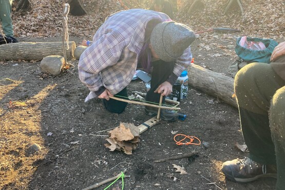 A person building a fire outdoors using a bow drill.