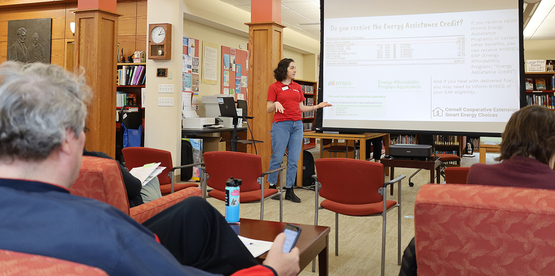 A person standing in front of a presentation screen, speaking with a small audience.