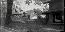 Vintage photo of a house growing with ivy behind a lawn and tree.