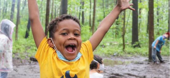 A young person in an outdoor setting holds their hands up in celebration!