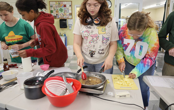 Several youth at a table together, with ingredients and cooking utensils.