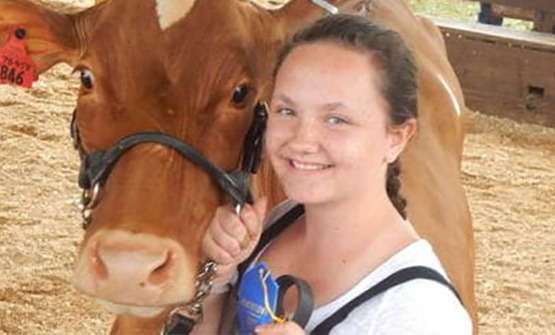 Young woman with dairy cow in arena at 4-H dairy program event