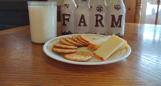 glass of milk with plate of cheese and crackers. Farm flower pot with daffodils. 