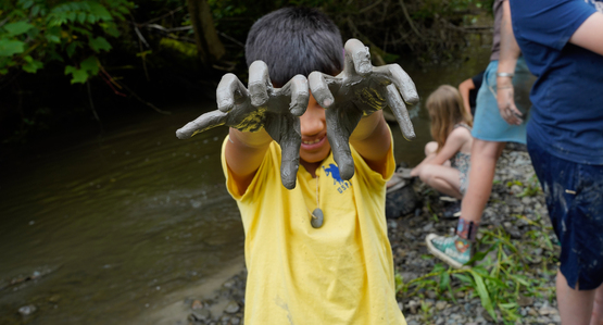 A child holding up his clay covered hands like claws.