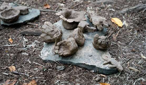 Clay formed into shapes of animals, bowls, and more drying on a flat rock.