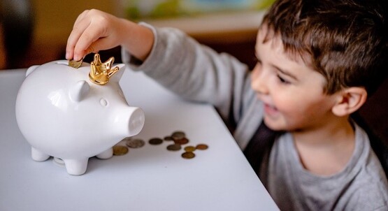 Kid adding coins to piggy bank