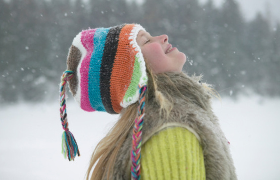 girl in a colorful knit hat with her face to the falling snow
