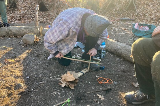 A person building a fire outdoors using a bow drill.