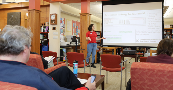 A person standing in front of a presentation screen, speaking with a small audience.