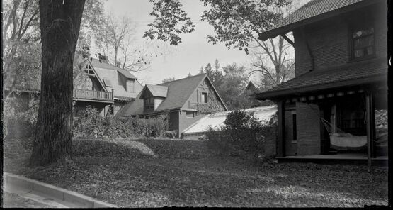 Vintage photo of a house growing with ivy behind a lawn and tree.